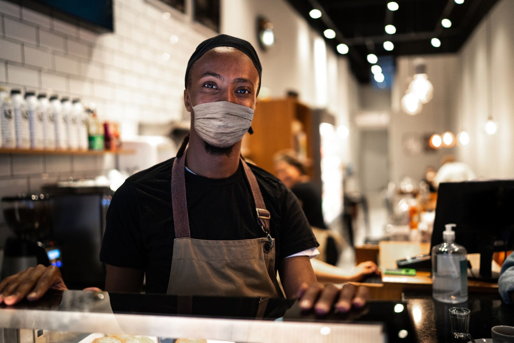 Portrait of young waiter with face mask in coffee shop